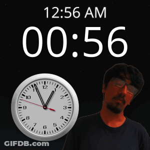 A Man With Glasses Stands In Front Of A Clock That Says 12:56 Am GIF