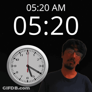 A Man With Glasses Stands In Front Of A Clock That Says 5:20 Am GIF