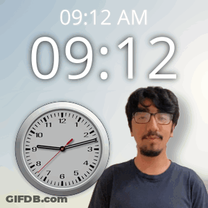 A Man With Glasses Stands In Front Of A Clock That Says 9:12 Am GIF