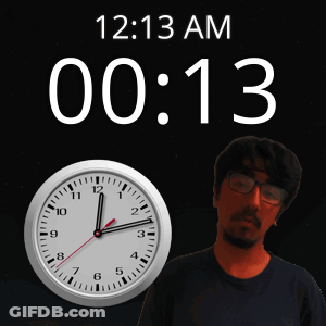 A Man With Glasses Stands Next To A Clock That Says 12:13 Am GIF