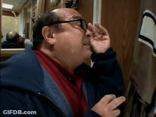 A Man With Glasses Wipes His Nose With His Hand In Front Of A Mirror GIF