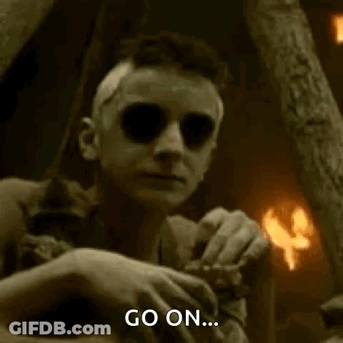 A Man With Glowing Eyes Is Sitting In A Dark Room With A Fire In The Background And Says `` Go On '' . GIF