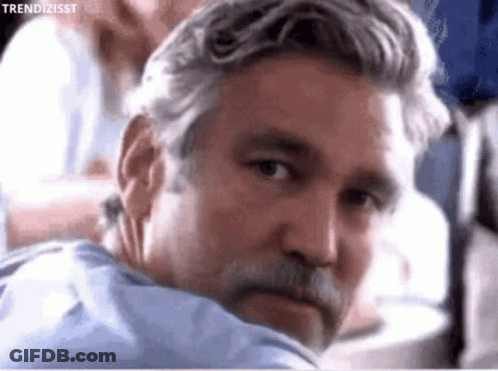 A Man With Gray Hair And A Beard Is Looking Over His Shoulder GIF