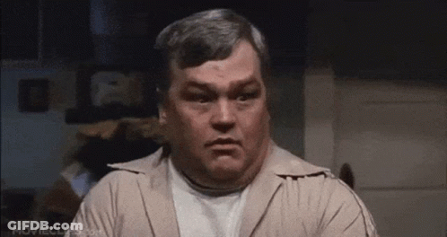 A Man With Gray Hair And A White Shirt Is Making A Face . GIF