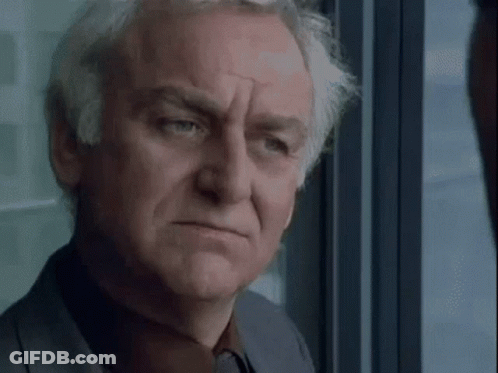 A Man With Gray Hair Is Looking Out Of A Window . GIF
