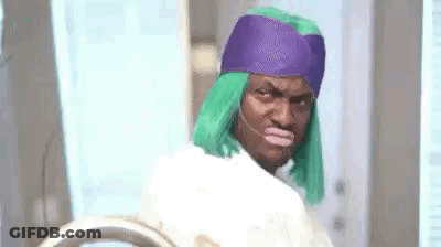 A Man With Green Hair And A Purple Headband Is Standing In Front Of A Washing Machine . GIF