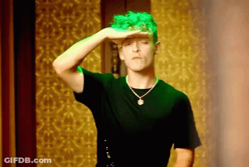A Man With Green Hair Is Wearing A Black Shirt And A Necklace And Covering His Eyes With His Hand . GIF