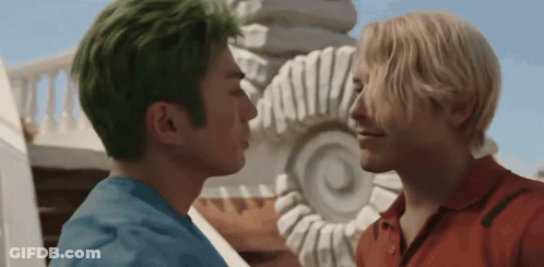A Man With Green Hair Kisses Another Man In Front Of A Statue GIF