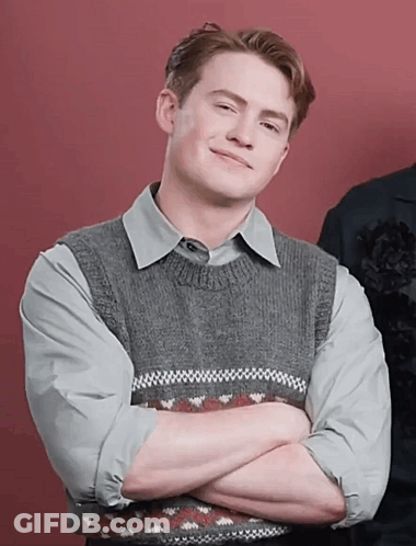 A Man With His Arms Crossed Is Wearing A Grey Sweater Vest GIF