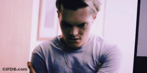 A Man With His Arms Crossed Is Wearing A Purple Shirt And A Gold Chain Around His Neck . GIF
