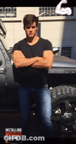 A Man With His Arms Crossed Standing In Front Of A Truck That Says Installing Muscles GIF