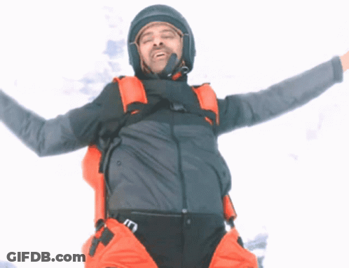 A Man With His Arms Outstretched Is Wearing A Gray Jacket And Orange Pants GIF