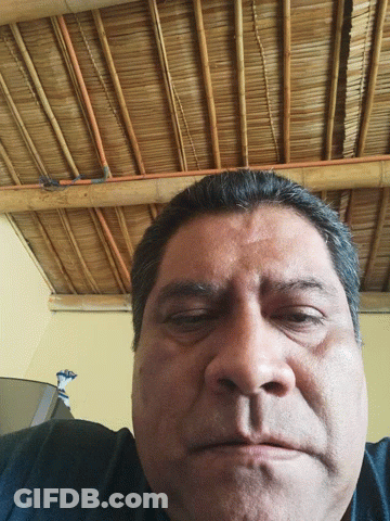 A Man With His Eyes Closed In Front Of A Straw Roof GIF