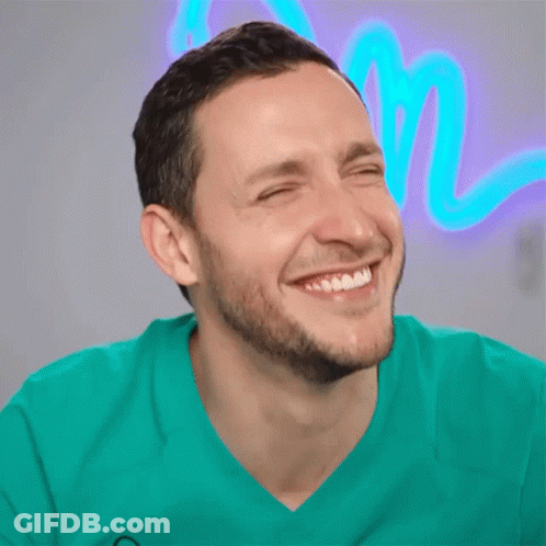 A Man With His Eyes Closed Is Smiling In Front Of A Neon Sign That Says M GIF
