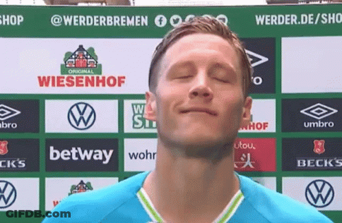 A Man With His Eyes Closed Stands In Front Of A Sign That Says ' Wiesenhof ' On It GIF