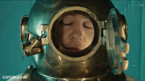 A Man With His Eyes Closed Wears A Helmet With A Round Window GIF