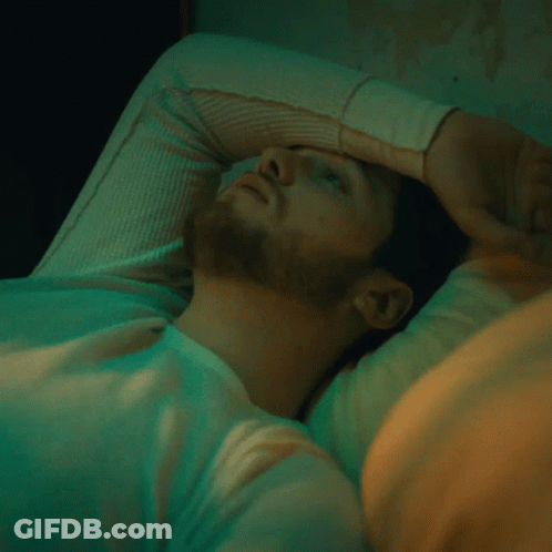 A Man With His Hand On His Forehead Is Laying In Bed GIF