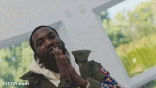 A Man With His Hands Folded In Front Of A Window With Trees Behind Him GIF
