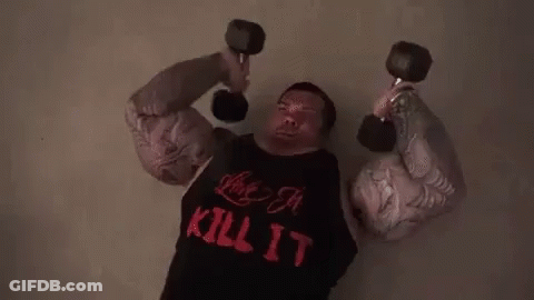 A Man With Huge Muscles Is Lifting Dumbbells While Wearing A Kill It Shirt . GIF