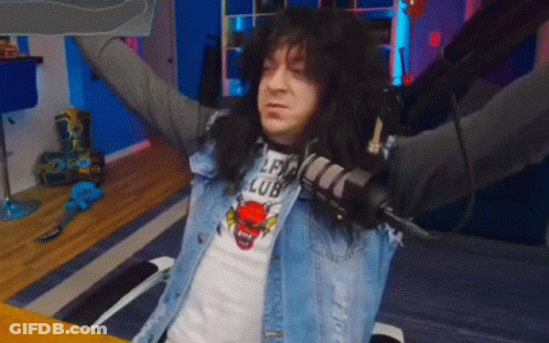 A Man With Long Black Hair Is Sitting At A Table With His Arms Outstretched And Holding A Microphone . GIF