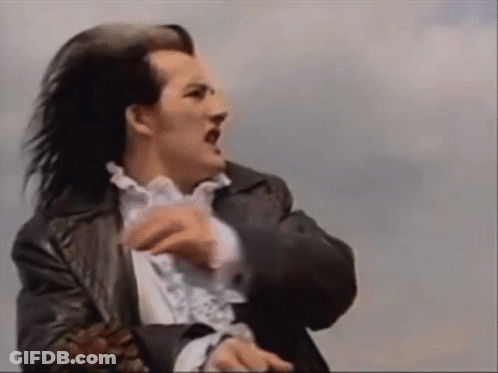 A Man With Long Black Hair Is Wearing A Black Jacket And A White Shirt . GIF