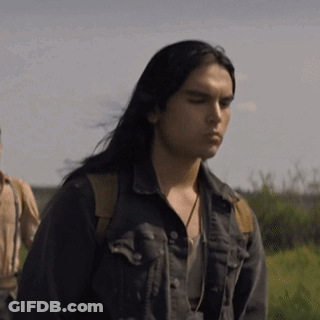 A Man With Long Black Hair Is Wearing A Denim Jacket And Standing In A Field . GIF