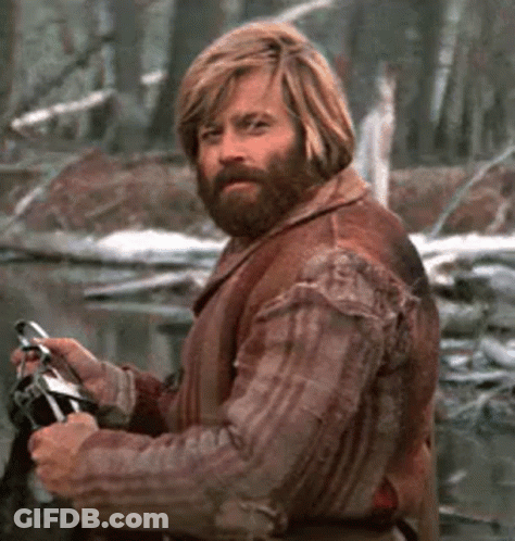 A Man With Long Blonde Hair And A Beard Is Holding A Fishing Rod In The Woods . GIF