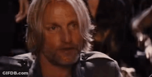 A Man With Long Blonde Hair And A Beard Is Sitting In A Dark Room With Other People . GIF