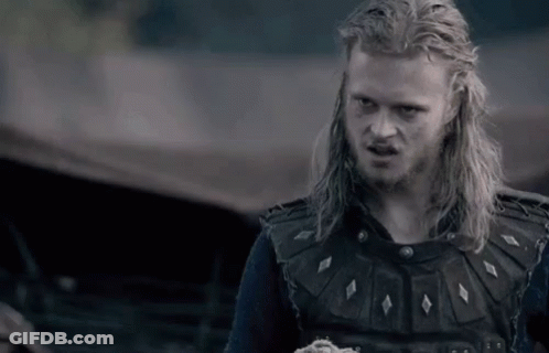 A Man With Long Blonde Hair And A Beard Is Wearing A Black Vest And A Black Shirt . GIF