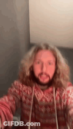A Man With Long Blonde Hair And A Beard Is Wearing A Red Sweater And Making A Funny Face . GIF