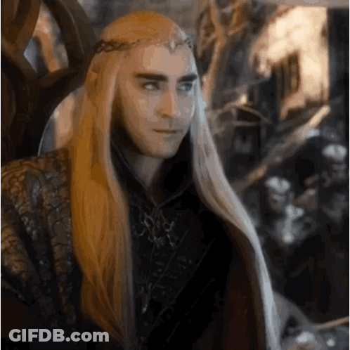 A Man With Long Blonde Hair And A Crown On His Head Is Sitting In A Throne . GIF
