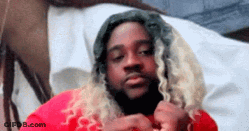 A Man With Long Blonde Hair And Dreadlocks Is Wearing A Red Shirt And Looking At The Camera . GIF