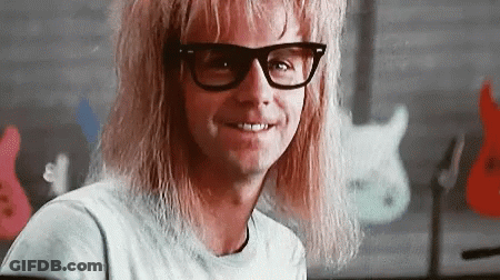 A Man With Long Blonde Hair And Glasses Is Smiling In A Classroom . GIF