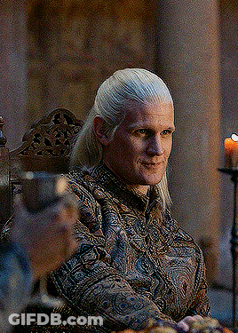 A Man With Long Blonde Hair Is Sitting In A Chair With A Candle In The Background . GIF