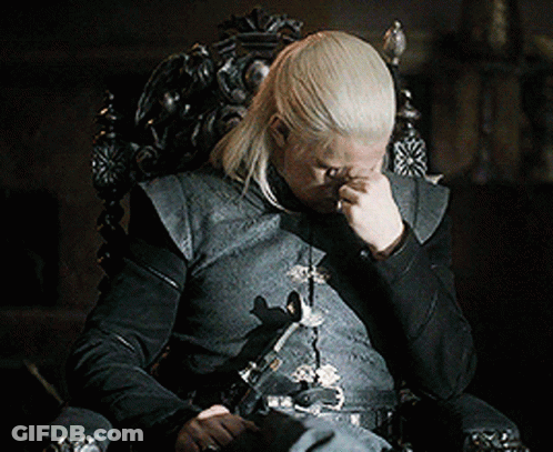 A Man With Long Blonde Hair Is Sitting In A Chair With His Hand On His Face GIF