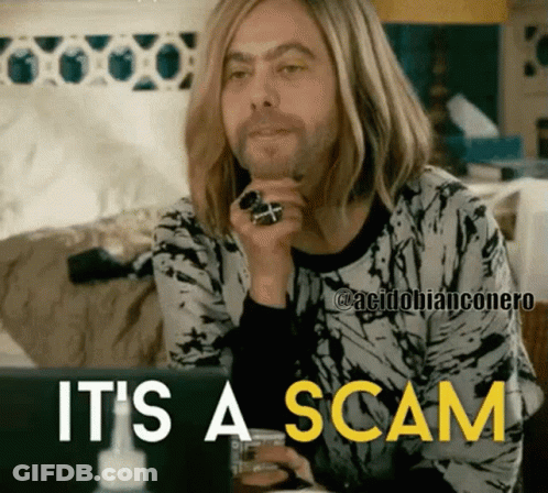 A Man With Long Blonde Hair Is Sitting In Front Of A Laptop With The Words " It 'S A Scam " Above Him GIF