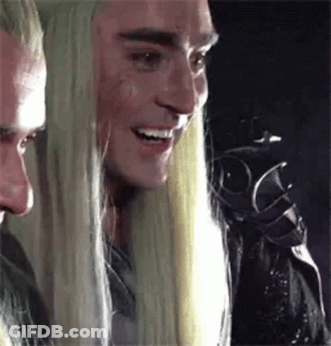 A Man With Long Blonde Hair Is Smiling And Looking At Another Man . GIF