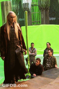 A Man With Long Blonde Hair Is Standing In Front Of A Green Background GIF