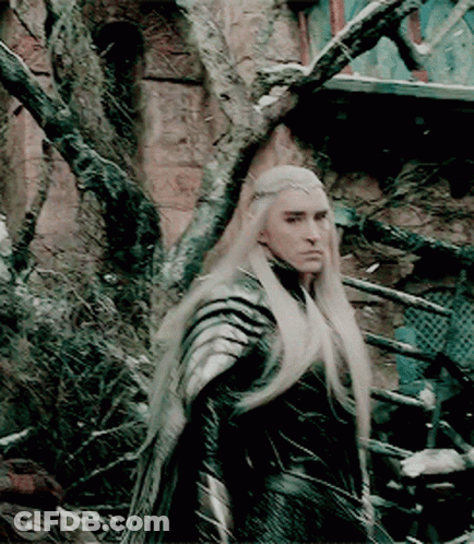 A Man With Long Blonde Hair Is Standing In Front Of A Tree GIF