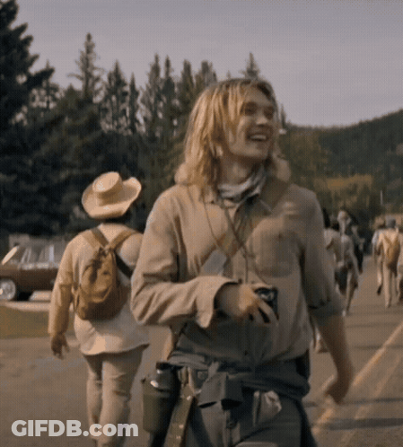 A Man With Long Blonde Hair Is Walking Down A Street With Other People GIF