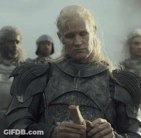 A Man With Long Blonde Hair Is Wearing Armor And Holding A Stick GIF