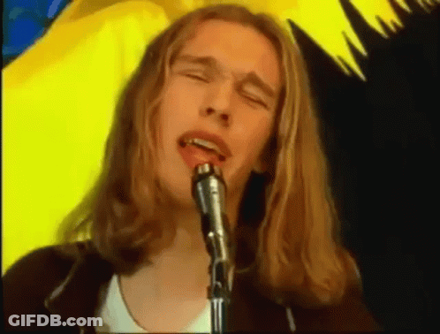 A Man With Long Blonde Hair Singing Into A Microphone GIF