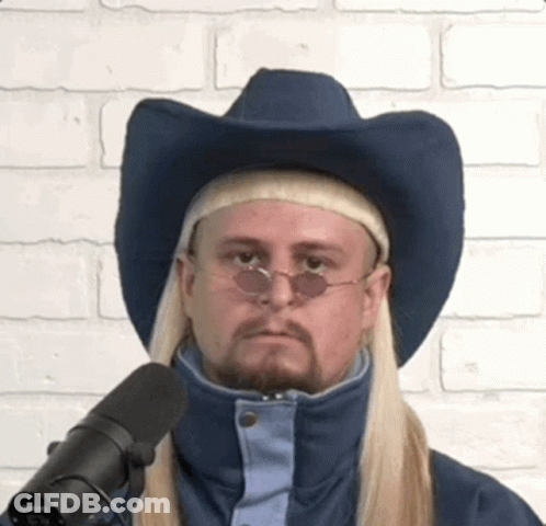 A Man With Long Blonde Hair Wearing A Cowboy Hat And Sunglasses Is Standing In Front Of A Microphone . GIF
