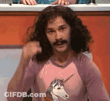 A Man With Long Curly Hair And A Mustache Is Wearing A Pink Unicorn Shirt . GIF