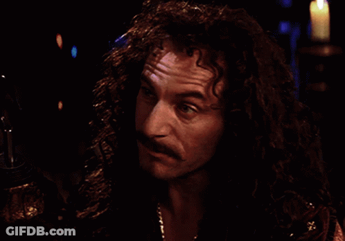 A Man With Long Curly Hair And A Mustache Looks At Something In The Dark GIF