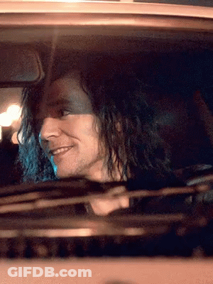 A Man With Long Curly Hair Is Driving A Car And Smiling GIF