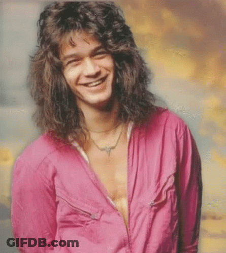 A Man With Long Curly Hair Is Smiling And Wearing A Pink Shirt GIF