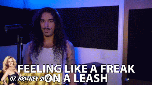 A Man With Long Curly Hair Is Standing In Front Of A Sign That Says " Feeling Like A Freak " GIF