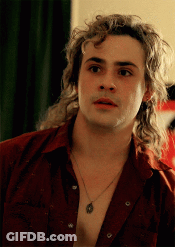 A Man With Long Curly Hair Is Wearing A Necklace And A Red Shirt GIF
