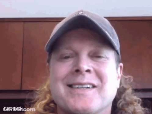 A Man With Long Curly Hair Wearing A Hat And Smiling With The Name Tony Little On The Bottom GIF